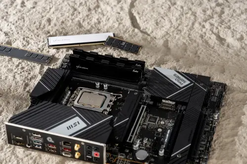 DDR RAM modules resting on sand beside a motherboard.